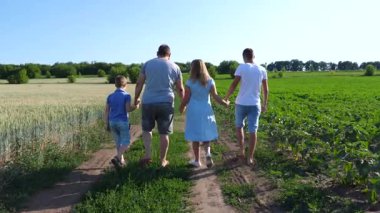 İki oğlu olan genç ebeveynler tarlaların yakınındaki kırsal yolda el ele yürüyorlar. Anne ve baba ve çocuklar yeşil çayırların yakınındaki yolda ilerliyorlar. Aile birlikte vakit geçiriyor.