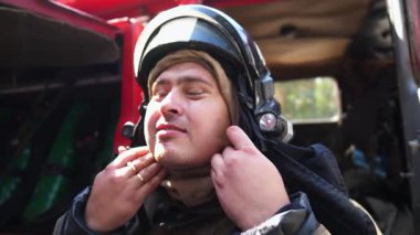 Young fireman in uniform putting oxygen mask against background of a big red truck. Male firefighter in full equipment near fire engine ready to work. Concept of saving lives and heroic profession.