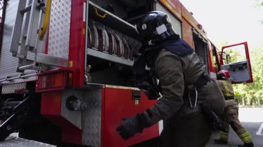 Profesyonel itfaiyeciler büyük kırmızı kamyondan malzeme çıkarıyorlar. Erkek itfaiyeciler yangını söndürmeye hazırlanıyor. Kahramanlık mesleği ve hayat kurtarma kavramı. Yavaşça kapat..