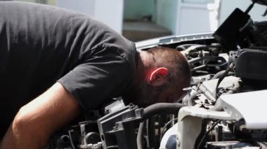 İş yerindeki bir arabanın motorunu kontrol eden profesyonel bir tamirci. Kaputun altında çalışan erkek oto tamircisi dışarıda motoru kontrol ediyor. Bakım ve otomobil kontrolü kavramı. Yavaş çekim.