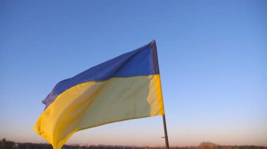Bayrak direğindeki Ukrayna bayrağı gökyüzünün arka planında rüzgara karşı dalgalanıyor. Ukrayna 'nın günbatımında kırsalda çırpınışının mavi-sarı sembolü. Rus saldırısına karşı barış ve destek kavramı.