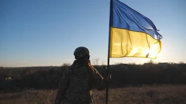 Kamuflaj üniformalı genç bir kız gün batımına karşı Ukrayna bayrağı sallıyor. Ukrayna ordusunun kadın askeri doktoru sahaya mavi-sarı bayrak kaldırıyor. Rus saldırısına karşı zafer.