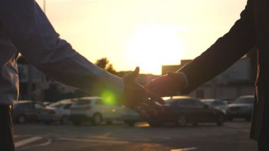 Dışarıda iş tokalaşması ve arka planda güneş ışığı. Erkek kollarını dışarıda sallıyor. Şehir ortamında birbirini selamlayan iki iş adamı. Meslektaşlar şehirde buluşup el sıkışırlar. Kapat..