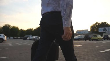 Sunrice saatinde otoparkta yürüyen evrak çantalı genç bir işadamı. İşe gidip gelen bir iş adamı. Kendine güveni tam bir adam sabah ofisine gidiyor. Yavaş çekim. Yakın çekim..