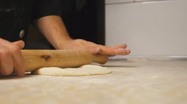 Lokantadaki mutfak masasında merdane kullanarak hamur işi açarken kollarını kapat. Aşçının erkek elleri mutfakta ahşap bir yüzeye hamur döküyor. Pizza yapma süreci. Yavaş çekim.