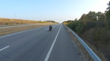 Sonbahar otobanında motosiklet süren motosikletliyi takip edin. Motosikletli, kır yolunda motosikletiyle yarışıyor. Yolculuk sırasında bisiklete binen adam. Özgürlük ve macera kavramı. Hava görüntüsü.
