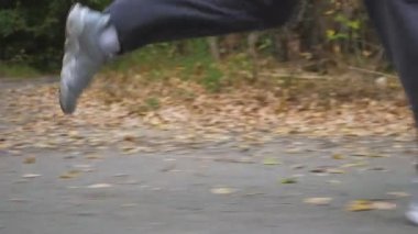 Sonbaharın başlarında ormanın yakınında yol boyunca koşan sportif bir adamın erkek ayakları. Genç atletin bacakları doğada patikaboyunca hızlı koşuyor. Dışarıda koşan güçlü bir adam. Sağlıklı aktif yaşam tarzı. Düşük görünüm.