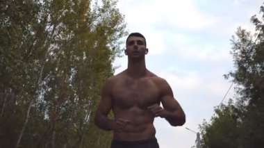 Kablosuz kulaklıklı yakışıklı sporcu arka planda güzel doğa manzarası olan yol boyunca koşuyor. Genç kaslı sporcu açık havada koşuyor. Sağlıklı aktif yaşam tarzı. Yakın çekim.