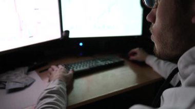 Erkek tüccar, akşamları emtiaları ve döviz çizelgelerini analiz ediyor. Geceleri birden fazla monitörü olan bir bilgisayar üzerinde çalışan genç bir finans analisti. Bitcoin BTC ve borsa kavramı.