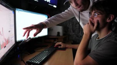 Hisse senetlerini ve döviz grafiklerini çoklu monitörlü bilgisayar kullanarak analiz eden iki genç simsar. Akşam vakti finans analistlerinin takım çalışması. Bitcoin BTC ve kripto ticareti kavramı. Yavaş çekim.