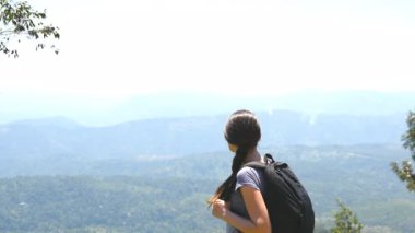 Sırt çantalı kadın yürüyüşçü arka planda kanyonla dağlarda yürüyor. Genç bayan turist güneşli bir günde patikaya çıkarken güzel doğanın tadını çıkarıyor. Yaz seyahati kavramı. Yavaş çekim.