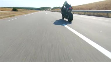 Anayolda motosiklet süren motosikletliyi takip edin. Motosikletli, kır yolunda motosikletiyle yarışıyor. Yolculuk sırasında bisiklet süren adam. Yolculukta özgürlük ve macera kavramı. Hava görüntüsü.