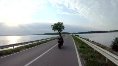 Motosikletli modern spor motosikletli göl kenarındaki yolda. Motosikletli yarış motosikleti yaz günü baraj yolunda. Nehir köprüsünden bisikletle geçen bir adam. Özgürlük ve yaşam tarzı kavramı.
