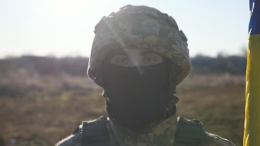 Kasklı ve kar maskeli asker kahverengi gözlü erkek Ukraynalı dışarıdaki kameraya bakıyor. Kırsal kesimde ulusal bayrağı olan genç bir askerin portresi. Ukrayna topraklarının işgali kavramı.