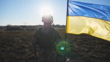 Kamuflaj üniformalı genç adam Ukrayna bayrağı sallıyor. Ukrayna ordusunun erkek askeri sahada mavi-sarı bayrağı kaldırıyor. Rus istilasına direniş. Yavaş çekim
