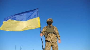 Askeri üniformalı Ukraynalı asker ulusal bayrağı kaldırıyor. Genç erkek asker mavi gökyüzüne karşı Ukrayna bayrağı sallıyor. Rus saldırısına karşı zafer. İstila direnişi. Düşük görünüm.