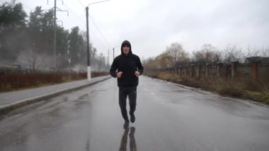 Bulutlu bir günde spor kıyafetli güçlü bir atlet patika boyunca koşuyor. Yağmurda asfalt yolda koşan genç sporcu. Atletik sporcu dışarıda kardiyo eğitimi alıyor. Sağlıklı aktif yaşam tarzı kavramı.