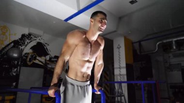 Modern spor salonundaki paralel barlarda şınav çeken güçlü bir sporcu. Spor salonunda spor yapan genç üstsüz bir sporcu. Kaslı sporcu sıkı çalışıyor. Sağlıklı ve aktif yaşam tarzı konsepti. Kapat..