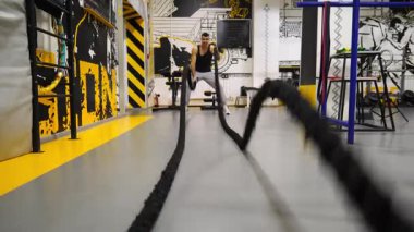 Genç kaslı sporcu eğitimi modern spor salonunda savaş halatları ile. Spor salonunda spor yapan güçlü bir adam. Atletik adam sıkı ve yoğun idman yapıyor. Spor ve aktif yaşam tarzı kavramı.