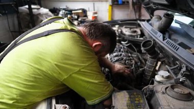 Yetişkin oto tamircisi atölyede arabanın bakımını yapıyor. Garajda kaputun altında çalışan profesyonel bir tamirci. Erkek tamirci iş yerinde otomobil motorunu kontrol ediyor. Aktarım tanısı.