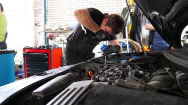 Araç kaputunun altında çalışan genç bir tamirci. Profesyonel oto tamircisi atölyedeki tornavida aletini kullanarak arabanın motorunu tamir eder. Erkek tamirci garajdaki otomobil motorunu kontrol ediyor. Yavaş çekim.