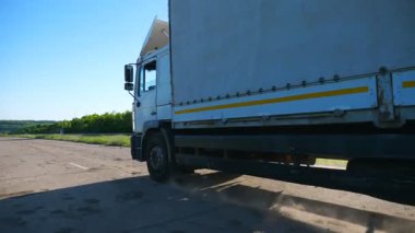 Boş otoban boyunca giden ve malları taşıyan kargo karavanı olan kamyonun yan görüntüsü. Kamyon kırsal yoldan geçerek hedefe gidiyor. Kargo taşıma konsepti. Yavaş çekim.