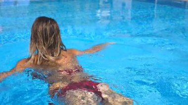 Young tanned woman in bikini swimming in pool of hotel at sunny day. Unrecognizable sexy girl relaxing during summer vacation refreshing in basin. Concept of travel or holiday. Slow motion Close up.