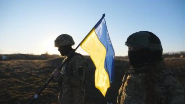 Ukrayna bayrağıyla yürüyen Ukrayna ordusunun kadın ve erkek askeri. Askeri üniformalı genç kadın ve adam gün batımında çayırda mavi-sarı pankartıyla gidiyorlar. Rus işgaline direniş.