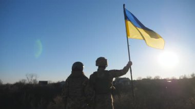 Ukrayna ordusunun kadın ve erkek askeri tepenin zirvesinde mavi-sarı pankartıyla dikiliyor. Askeri üniformalı genç kız ve adam Ukrayna bayrağını güneşli mavi gökyüzüne kaldırdı. Dolly vurdu..