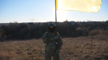 Kamera, Ukrayna bayrağını dalgalandırmış askeri üniformalı bir kızı gösteriyor. Kadın Ukraynalı asker, Rus saldırısına karşı zafer sembolü olarak ulusal bayrak sallıyor..