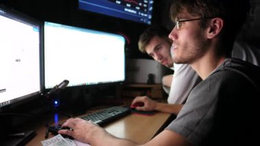 Hisse senetlerini ve döviz grafiklerini çoklu monitörlü bilgisayar kullanarak analiz eden iki genç simsar. Akşam vakti finans analistlerinin takım çalışması. Bitcoin BTC ve kripto ticareti kavramı. Yavaş çekim.