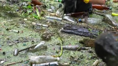 Koruyucu eldivenli kadın çevrecilerin elleri enkaz nehirlerini temizliyor. Kirli gölde plastik şişe toplayan kauçuk elbiseli tanınmayan gönüllüler. Çevre kirliliği koruması.
