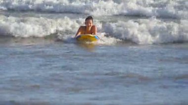 Güzel bir kadın yaz gezisi sırasında sörf tahtasındaki okyanus dalgalarında yüzer. Mutlu genç kız güneşli bir günde sörf yapmayı öğreniyor. Tatil ya da tatil kavramı. Yavaş çekim.