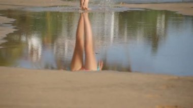 Çıplak ayaklı genç kadın, büyük okyanus suyu birikintisine ve deniz kıyısına yakın basamaklara yansıyor. Dişi bacaklar, sahil kenarındaki boş tropik sahil boyunca yürüyor. Yaz tatili ya da tatil konsepti. Yavaş çekim.