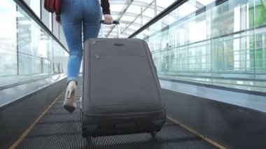 İş kadını onun Bagaj ile terminal salonu geçmekte bacaklar. Yüksek topuklar üzerinde yürüyen merdiven ve rulo bavul tekerlekleri üzerinde yürüyen genç kız. Bayan seyahat ya da iş gezisi devam ediyor. Ağır çekim.