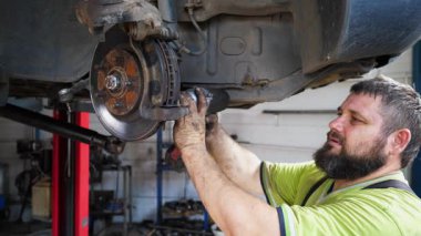 Erkek tamirci garajdaki özel elektrikli aletle vidaları söküyor. Profesyonel oto tamircisi atölyedeki kaldırma aracının altında çalışır. Otomobili tamir eden yetişkin tamirci..