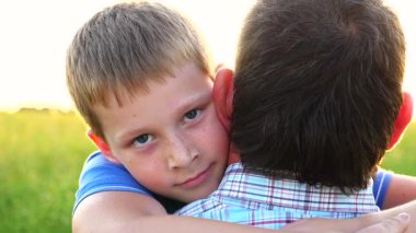 Küçük çocuk kameraya bakıyor ve arka planda parlak güneş ışığına karşı babasına sarılıyor. Kırsalda küçük oğlunun elini tutan genç bir baba. Aile mutluluğu kavramı. Yavaşça kapat..
