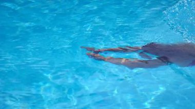 Saydam berrak suyla havuzda yüzen tanınmayan bir kadın. Genç kız yaz tatilinde otel havzasında yüzüyor. Yaz tatili kavramı. Yavaş çekim kenar görünümü.
