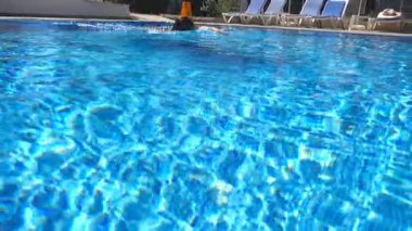 Güneşli bir günde mavi berrak suyla boş havuzda yüzen genç bir kadın. Yaz tatilinde dinlenen kız havuzda dinleniyor. Bayan dinlenme tesisinde eğleniyor. Seyahat ya da tatil kavramı. Yavaş çekim.