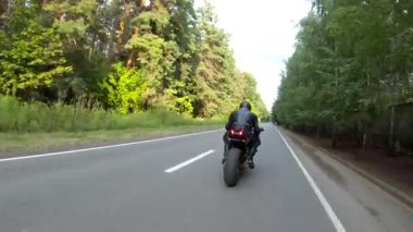Orman yolunda motosiklet yarışı yapan bir motosikletli. Ormanın yakınındaki kırsal yolda kasklı bir adam spor motosikletine biniyor. Yolculuk sırasında bisiklet süren adam. Özgürlük ve macera kavramı. Hava görüntüsü.