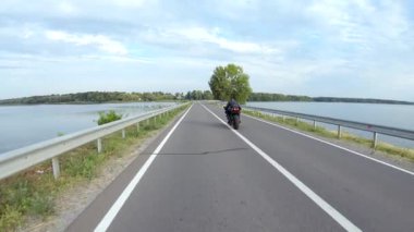 Motosikletli modern spor motosikletli göl kenarındaki yolda. Motosikletli, yaz günü baraj yolunda motosikletiyle yarışıyor. Yolculuk sırasında bisiklet süren bir adam. Özgürlük ve macera kavramı. Hava görüntüsü.