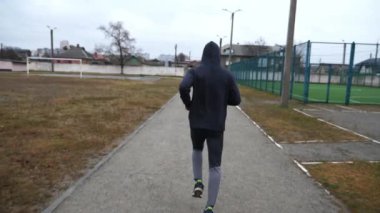 Atletik sporcu, bulutlu bir günde okul stadyumunda koşuyor. Genç sporcu atletizm sahasında koşuyor. Spor giyim bölümünde dışarıda egzersiz yapan güçlü bir adam. Aktif sağlıklı yaşam tarzı.