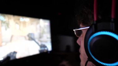 Genç adam geceleri bilgisayarda birinci şahıs nişancı olarak oynuyor. Kulaklık takan erkek oyuncu evde bilgisayar başında online video oyunu oynuyor. Siber uzay, rekabet ve turnuva kavramı. Yavaş çekim.