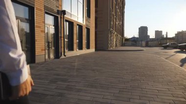 Şehir caddesinde evrak çantalı başarılı bir iş adamının arka görüntüsü. Resmi kıyafetli genç girişimci kaldırımda işe gidiyor. Kendine güvenen bir erkek yönetici işe gidip geliyor. Yavaş çekim.