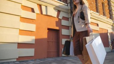 Zarif bir kadın şehir meydanında yürürken bütün kağıt paketleri taşıyor. Güzel elbiseli bayan müşteriler alışveriş sonrası alışveriş çantalarını kaldırıma koyuyorlar. Mevsimsel satış kavramı. Dolly vurdu..