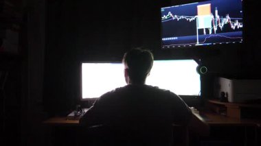 Trader engaged in cryptocurrency analysis, seated at a desk with dual monitors showcasing market data, capturing the intensity and focus of digital trading in a dimly lit environment