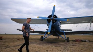 Pilot performing dynamic dance routine beside vintage blue airplane, showcasing energetic movements and engaging expressions, capturing the thrill of aviation and dance in a captivating outdoor scene