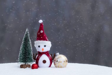 Noel Oyuncağı Kardan Adam: Karlı arka planda Noel süslemeleri olan atkı takmış eğlenceli bir kardan adam.