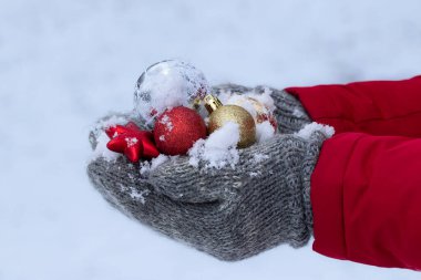 Parlak arka planda renkli Noel topları. Elleri sıcak eldivenlerde. Noel balolarını doğal karla tutarlar..