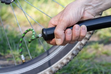 Yazın sokakta bisiklet tekerleği pompalayan bir adamın yakın çekimi. Adam pompa kullanarak bisiklet tekerleğini şişiriyor..